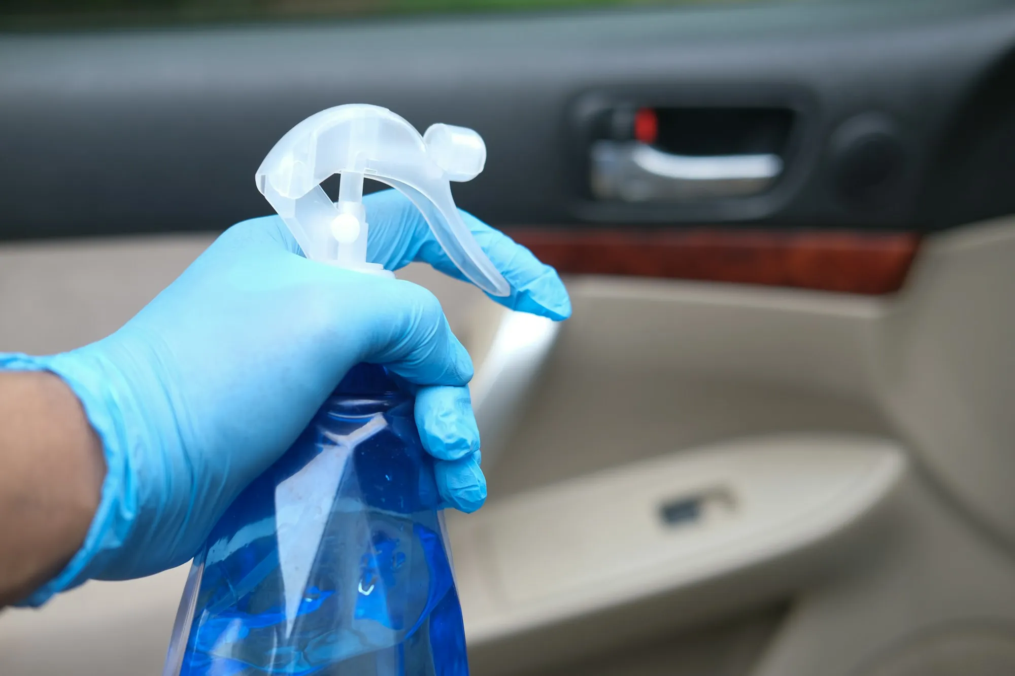 Gloved hand holding a spray bottle near a door handle